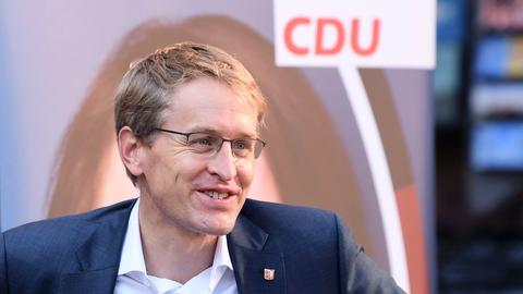 Daniel Günther blickt lächelnd an der Kamera vorbei, im Hintergrund ist ein CDU-Wahlplakat zu sehen