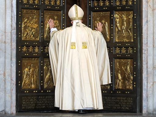 Papst Franziskus in weißem Gewand in der Rückansicht vor der Heiligen Pforte des Petersdoms im Vatikan, 8. Dezember 2015