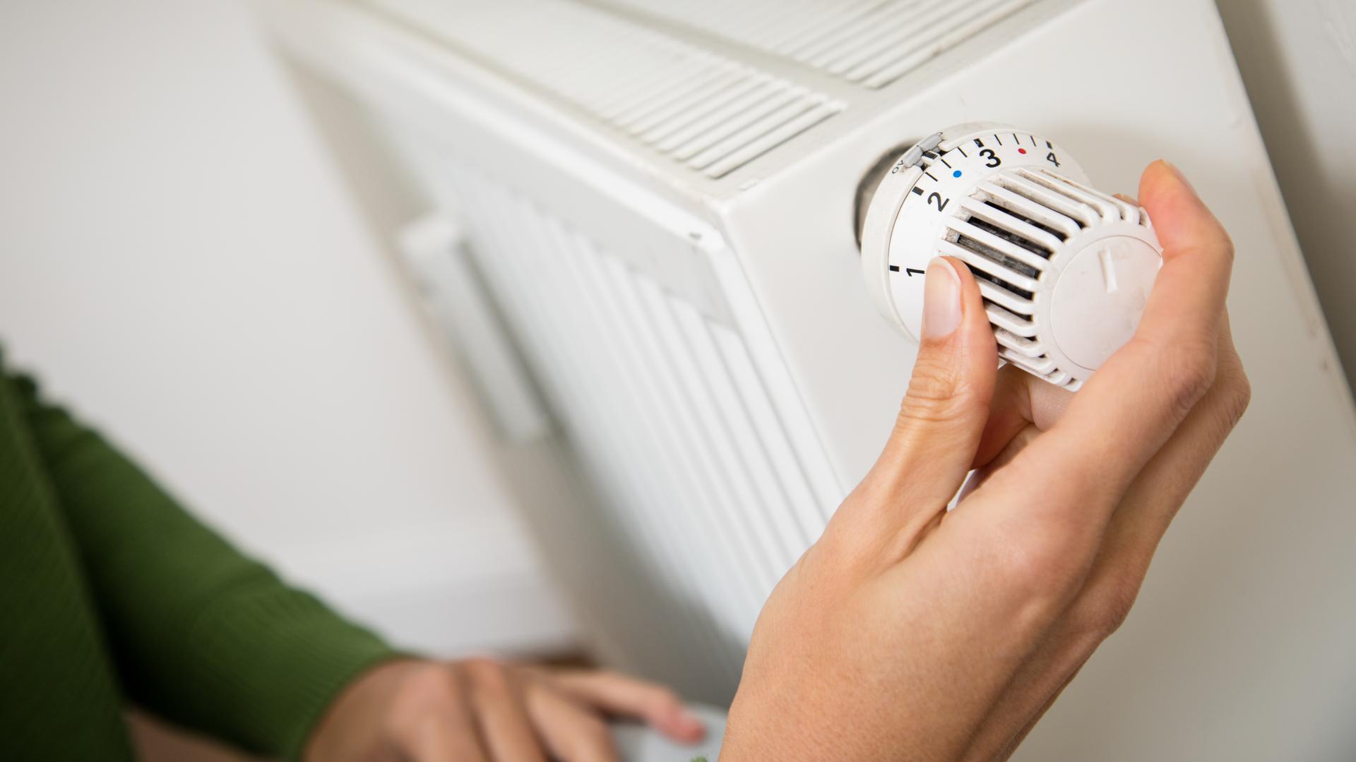 Eine Frau dreht am Regler der Heizung (gestellte Szene)