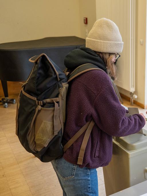 Eine junge Frau wirft ihren Wahlzettel in eine Wahlurne. Eine andere Frau beobachtet das.  