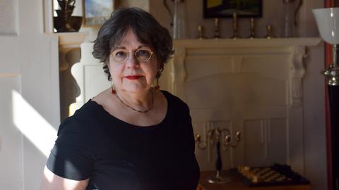 Elisabeth Bronfen schaut in die Kamera. Sie trägt ein schwarzes Oberteil und roten Lippenstift.