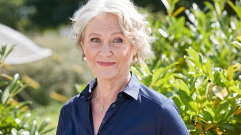 Edelgard Hansen trägt eine blaue Bluse, steht vor einem Busch und schaut freundlich in die Kamera. Edelgard Hansen trägt eine blaue Bluse, steht vor einem Busch und schaut freundlich in die Kamera.