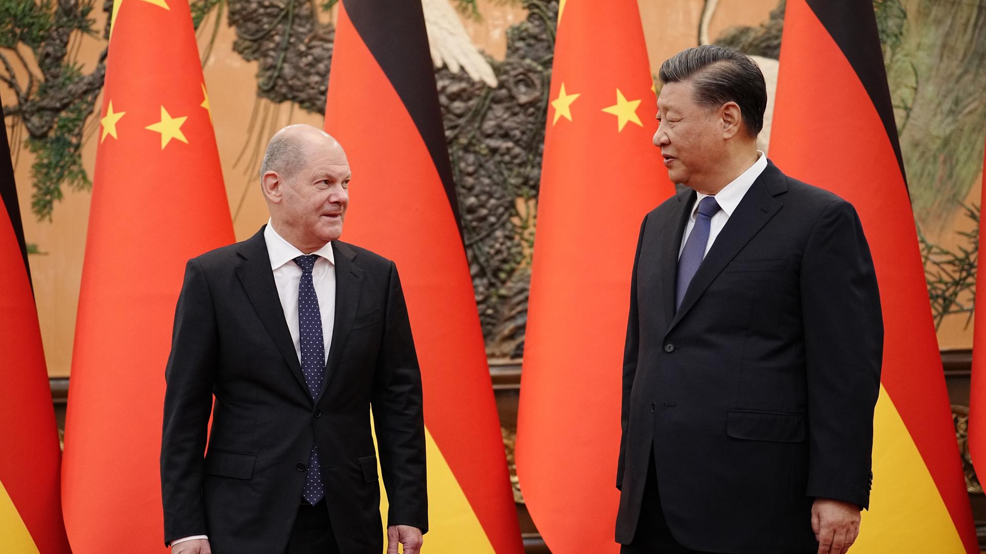 Chinas Präsident Xi Jinping (r) und Bundeskanzler Olaf Scholz (SPD) stehen vor Fahnen Chinas und der Bundesrepublik.