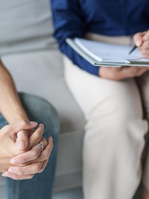 Im Gespräch mit einem Patienten macht eine Therapeutin sich Notizen. Beide Personen sind im Bildausschnitt so zu sehen, dass ihre Gesichter nicht zu erkennen sind.