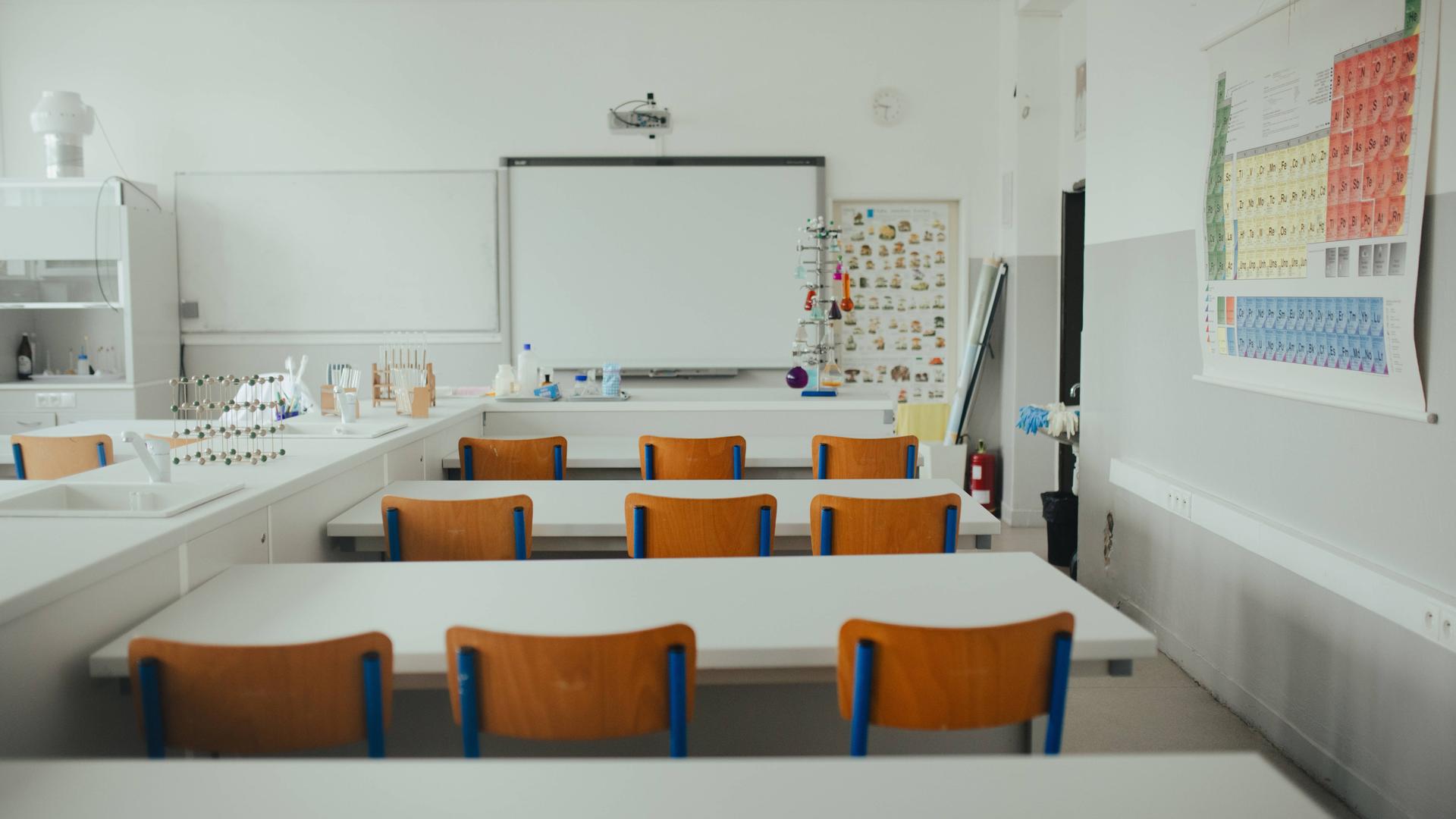 Blick in einen modernen weißen Klassenraum mit Holzstühlen und chemischen Modellen.