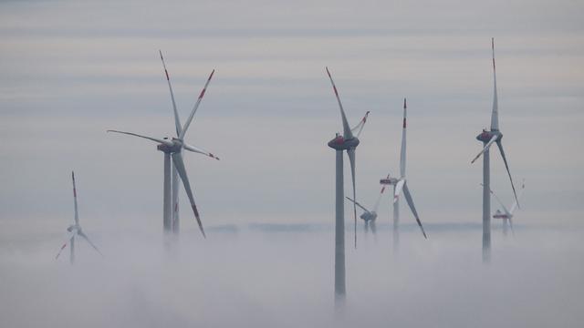 Windräder ragen aus einer dichten Nebelwand heraus.