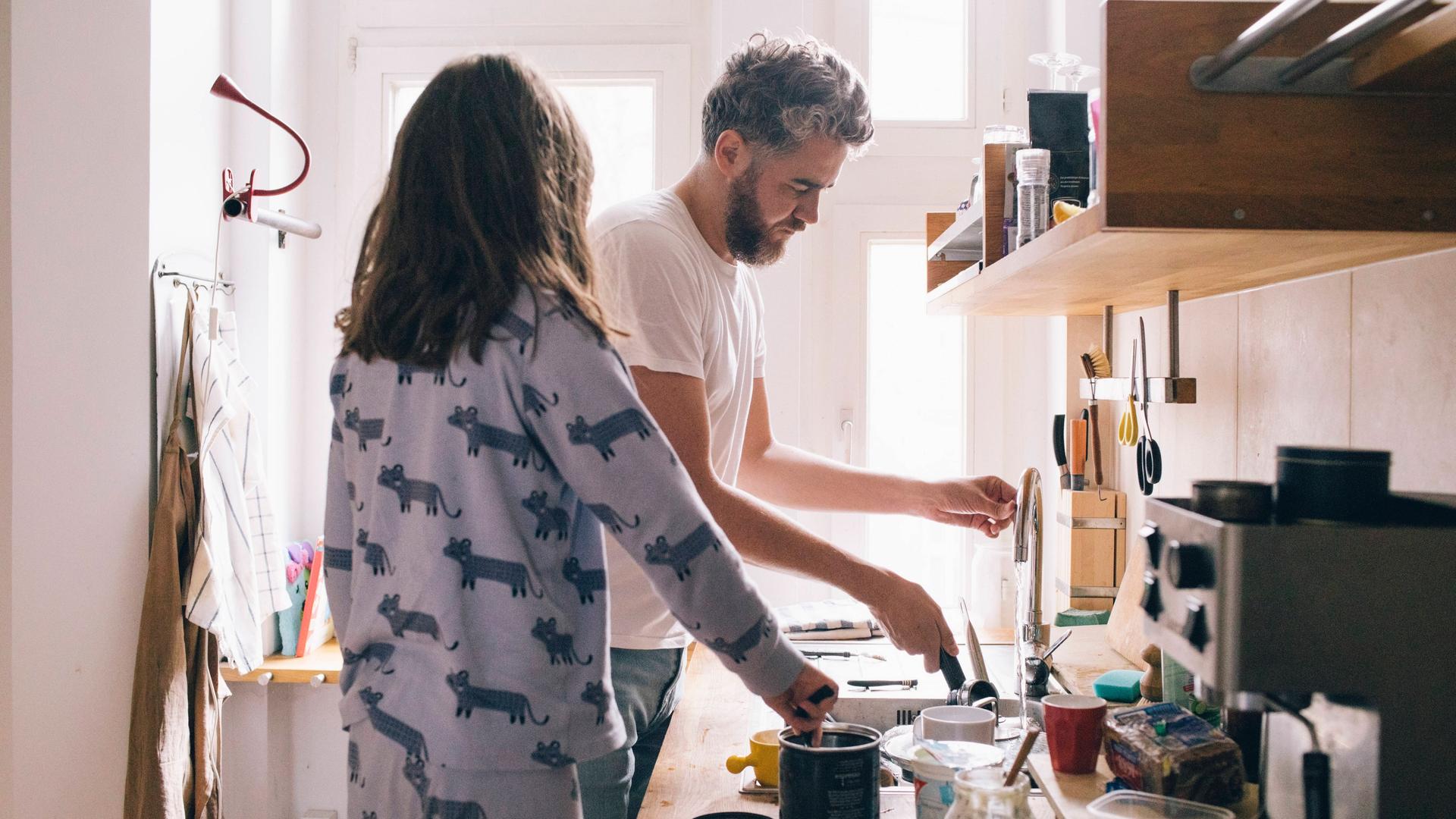 Ein Mann und eine Frau, noch in Schlaganzügen gekleidet, waschen gemeinsam in der Küche ab.
