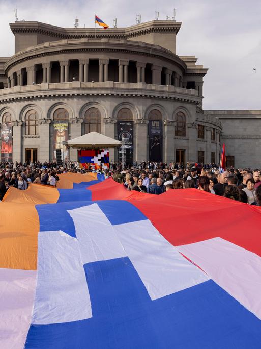 Menschen tragen eine große Flagge der Republik Arzach während einer Demonstration vor der Nationaloper in Yerevan. Menschen tragen eine große Flagge der Republik Arzach während einer Demonstration vor der Nationaloper in Yerevan.