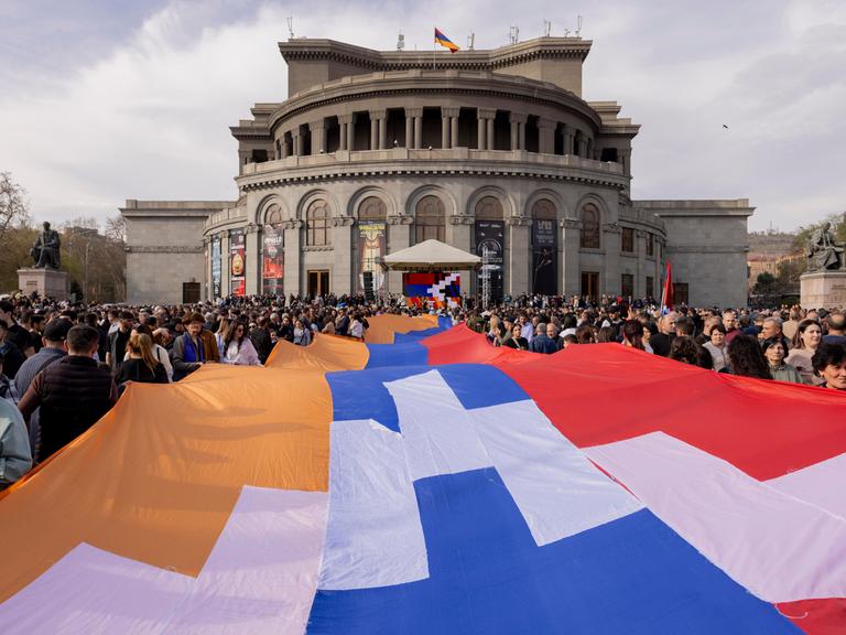 Menschen tragen eine große Flagge der Republik Arzach während einer Demonstration vor der Nationaloper in Yerevan. Menschen tragen eine große Flagge der Republik Arzach während einer Demonstration vor der Nationaloper in Yerevan.