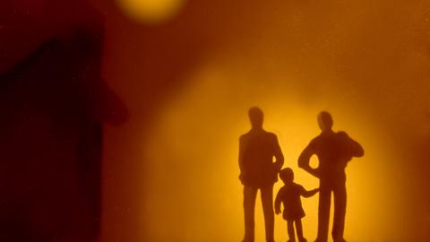 Die Silhouetten zweier Erwachsener, zwischen denen ein Kind steht. Die Silhouetten zweier Erwachsener, zwischen denen ein Kind steht.