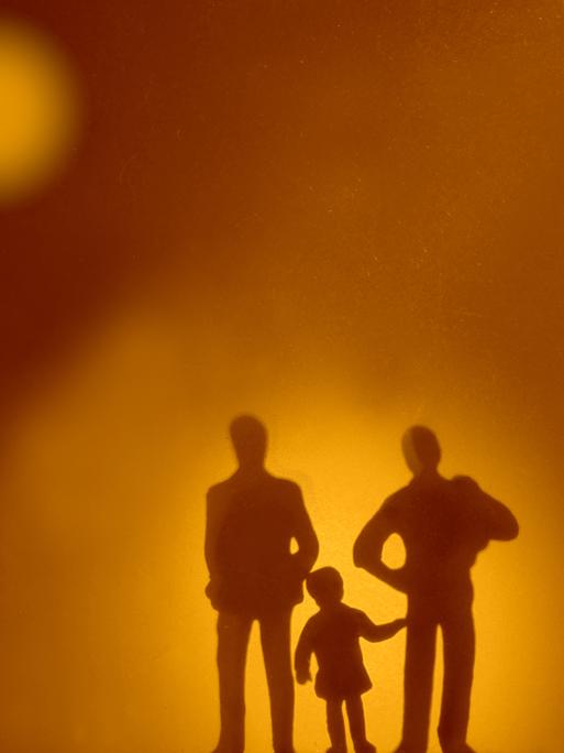 Die Silhouetten zweier Erwachsener, zwischen denen ein Kind steht.