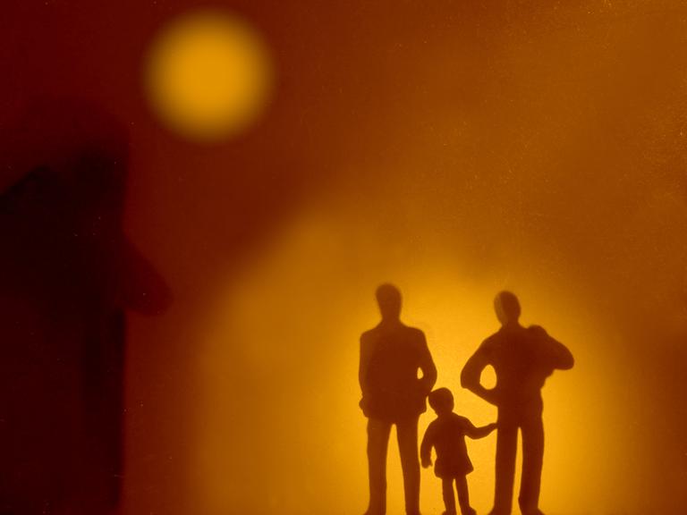 Die Silhouetten zweier Erwachsener, zwischen denen ein Kind steht.