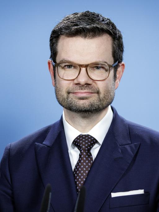 Porträt von Marco Buschmann. Der Minister trägt Anzug, Brille und Drei-Tage-Bart.