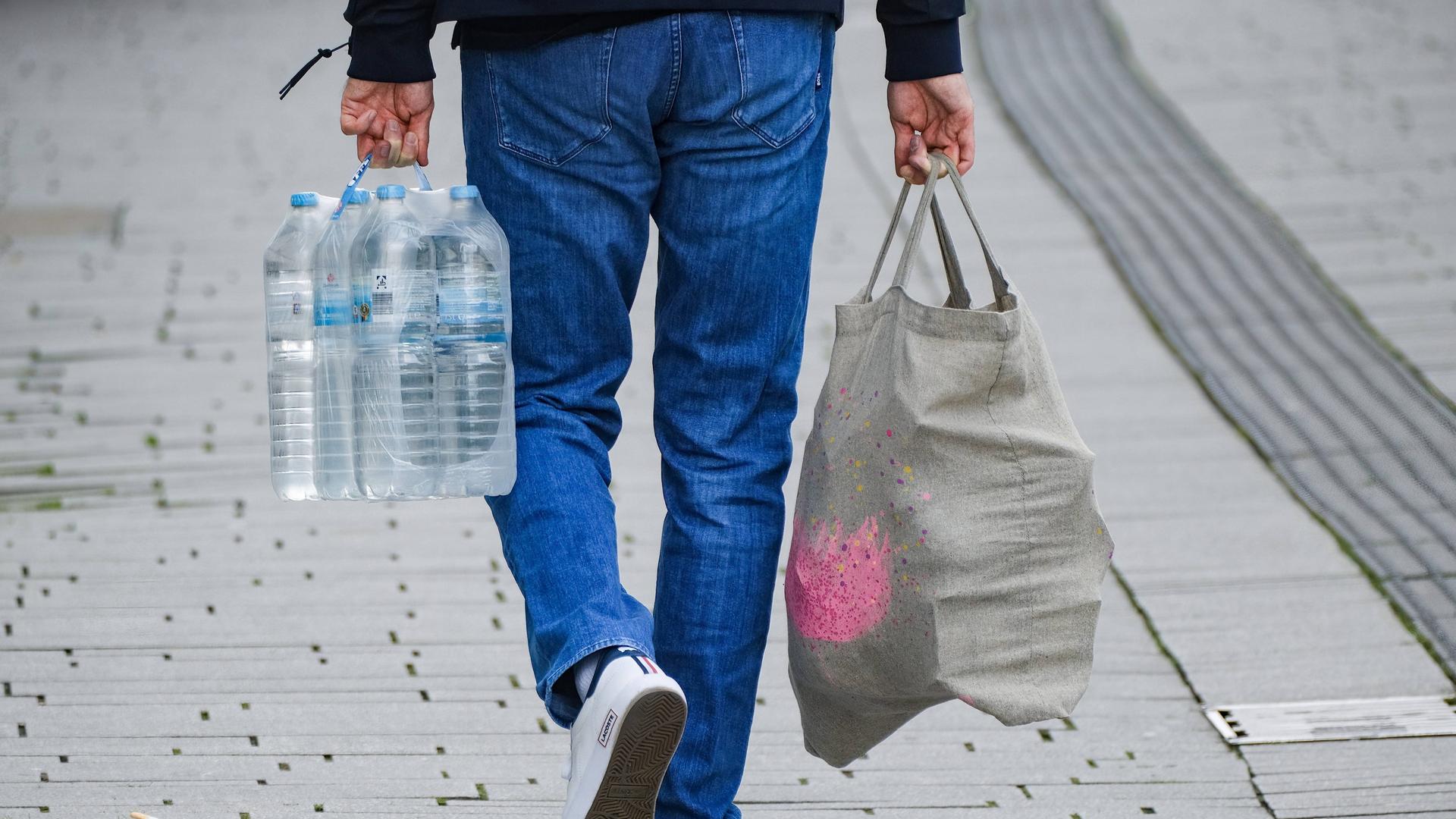 Mann mit Einkaufstüte und Sechserpack Wasserflaschen