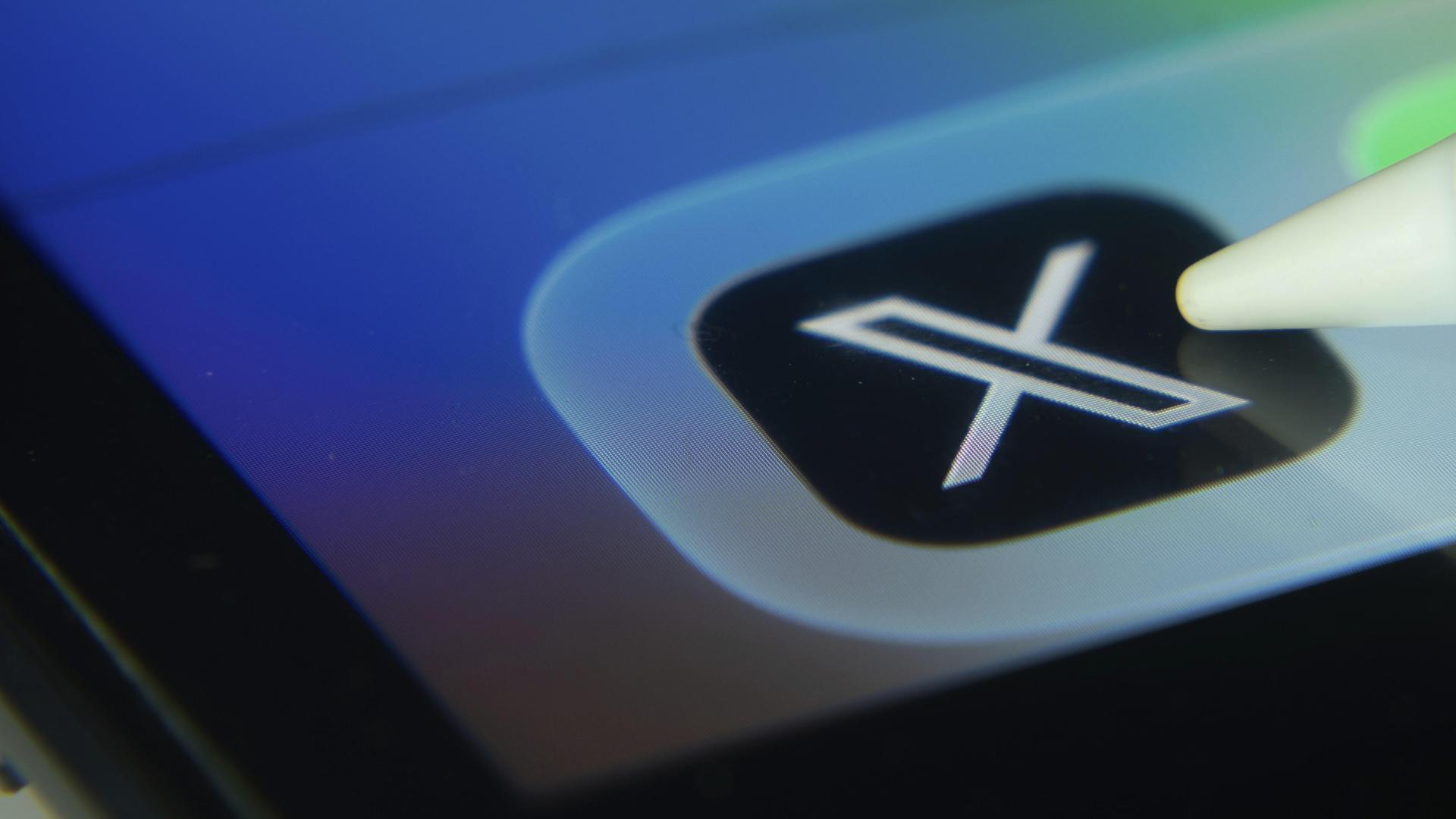 Eine Kugelschreiber zeigt auf einem Mobilfunk-Display auf die App der Plattform X. 
