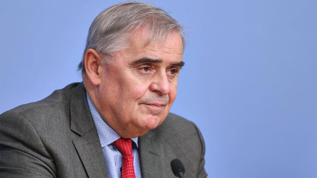 Peter Müller bei einer Pressekonferenz in einem grauen Anzug vor hellblauer Wand.