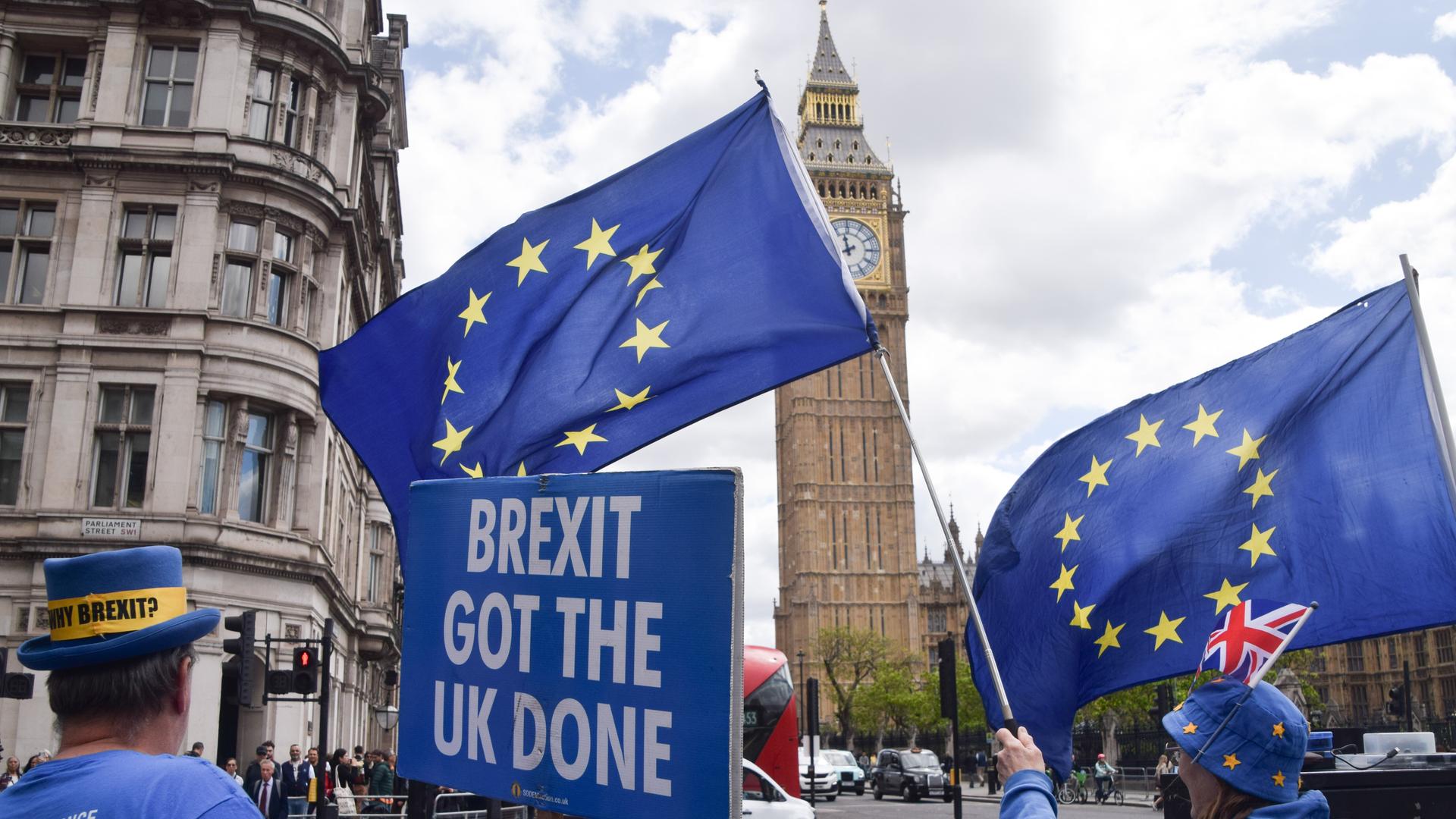 Vor dem britischen Parlament in London stehen proeuropäische Demonstrierende mit EU-Flaggen. Eine Person hält ein Schild mit der Aufschrift „Brexit got the UK done“. Vor dem britischen Parlament in London stehen proeuropäische Demonstrierende mit EU-Flaggen. Eine Person hält ein Schild mit der Aufschrift „Brexit got the UK done“.