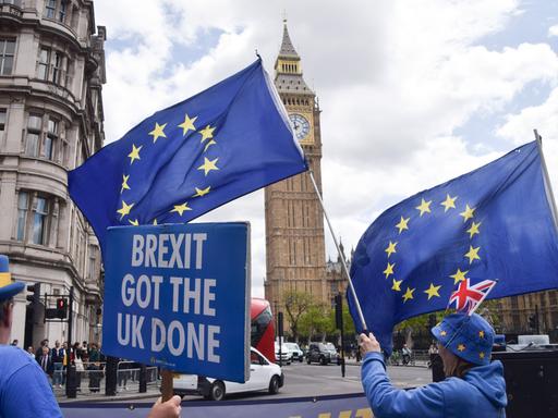 Vor dem britischen Parlament in London stehen proeuropäische Demonstrierende mit EU-Flaggen. Eine Person hält ein Schild mit der Aufschrift „Brexit got the UK done“. Vor dem britischen Parlament in London stehen proeuropäische Demonstrierende mit EU-Flaggen. Eine Person hält ein Schild mit der Aufschrift „Brexit got the UK done“.