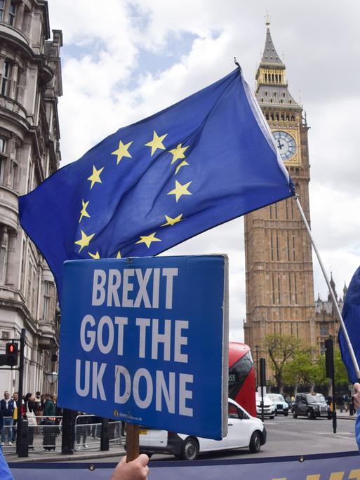 Vor dem britischen Parlament in London stehen proeuropäische Demonstrierende mit EU-Flaggen. Eine Person hält ein Schild mit der Aufschrift „Brexit got the UK done“. Vor dem britischen Parlament in London stehen proeuropäische Demonstrierende mit EU-Flaggen. Eine Person hält ein Schild mit der Aufschrift „Brexit got the UK done“.