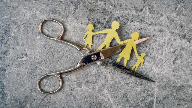 Ein Schere durchtrennt symbolisch eine Papierfamilie