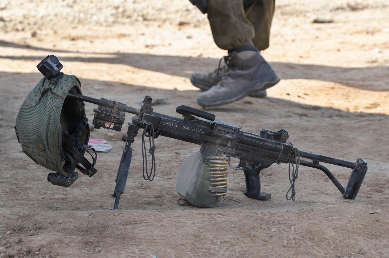 Der Helm eines israelischen Militärangehörigen hängt ruhend an seiner Waffe, während im Hintergrund ein Mensch vorbeiläuft.