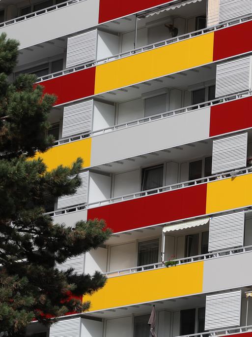 Hausfassade eines Mehrfamilienhausees mit gelber und roter Verkleidung an den Balkonen.