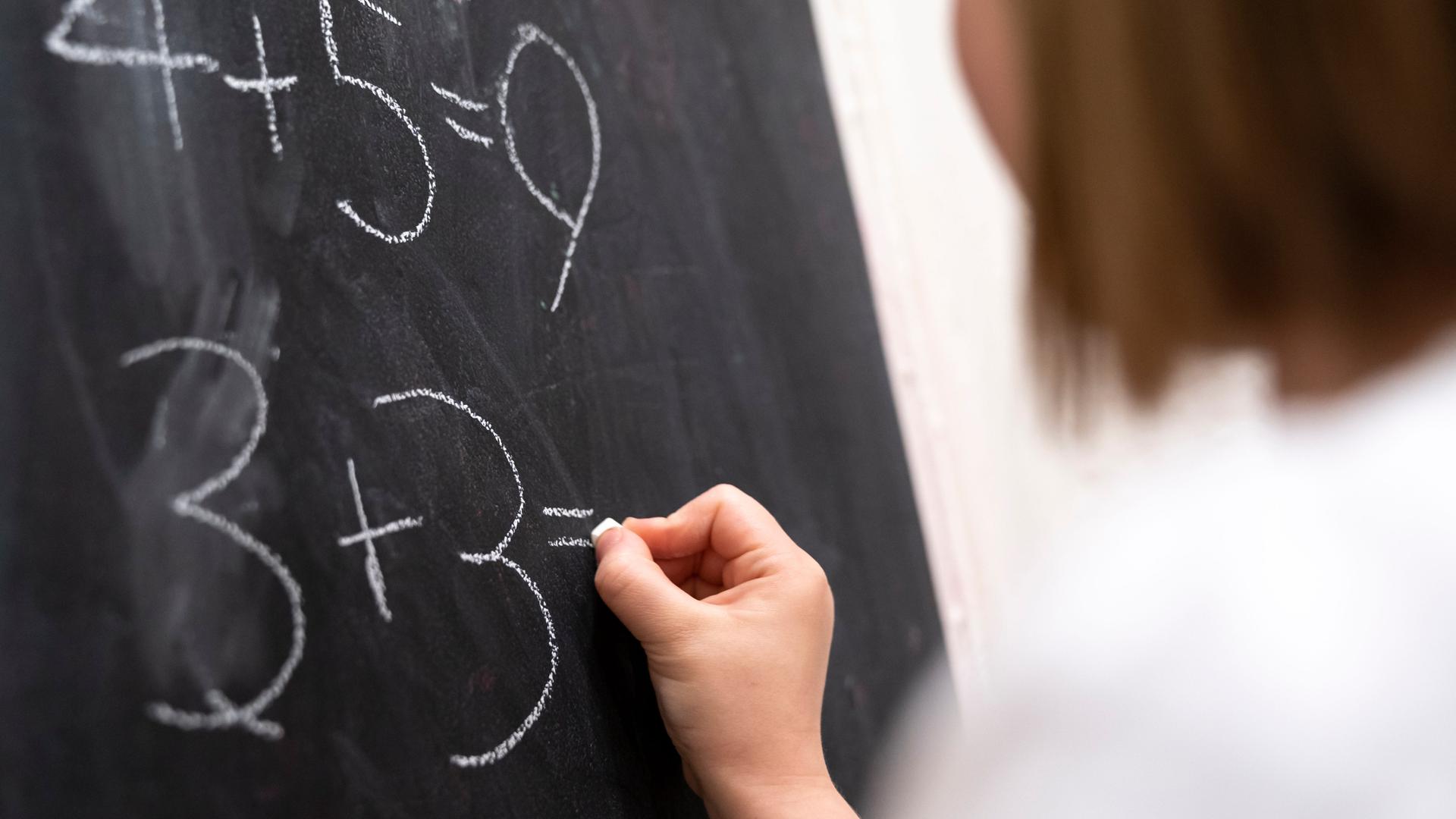 Eine Lehrerin schreibt eine Rechenaufgabe an die Tafel. Eine Lehrerin schreibt eine Rechenaufgabe an die Tafel.