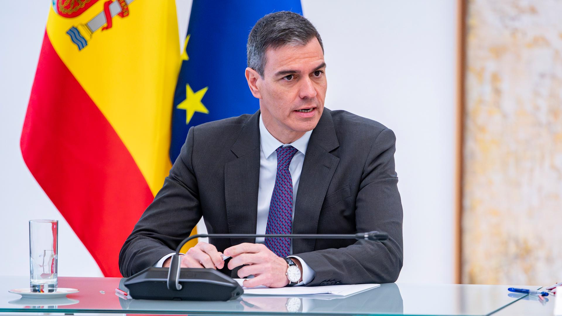 Der spanische Premierminister Pedro Sánchez steht in Anzug und Krawatte vor einem Rednerpult und spricht in ein Mikrofon.