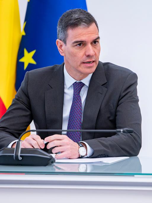 Der spanische Premierminister Pedro Sánchez steht in Anzug und Krawatte vor einem Rednerpult und spricht in ein Mikrofon.