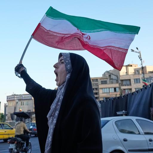 Eine Frau steht in den Straßen Teherans, hält die iranische Flagge in die Luft und ruft.