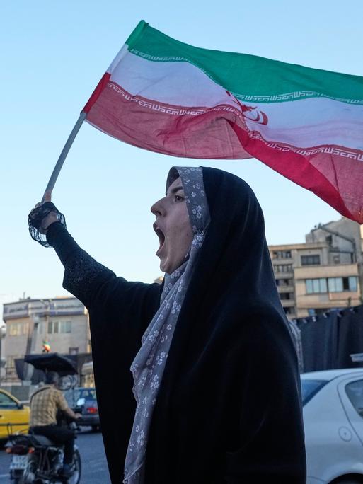 Eine Frau steht in den Straßen Teherans, hält die iranische Flagge in die Luft und ruft.