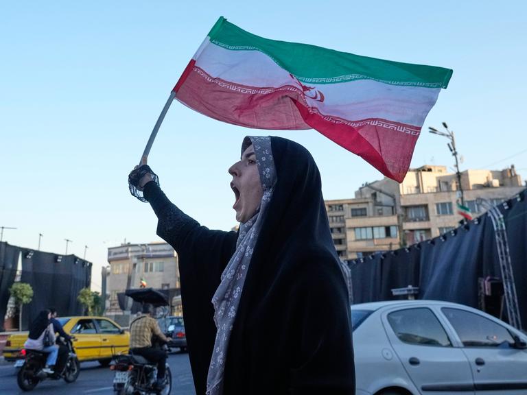 Eine Frau steht in den Straßen Teherans, hält die iranische Flagge in die Luft und ruft.