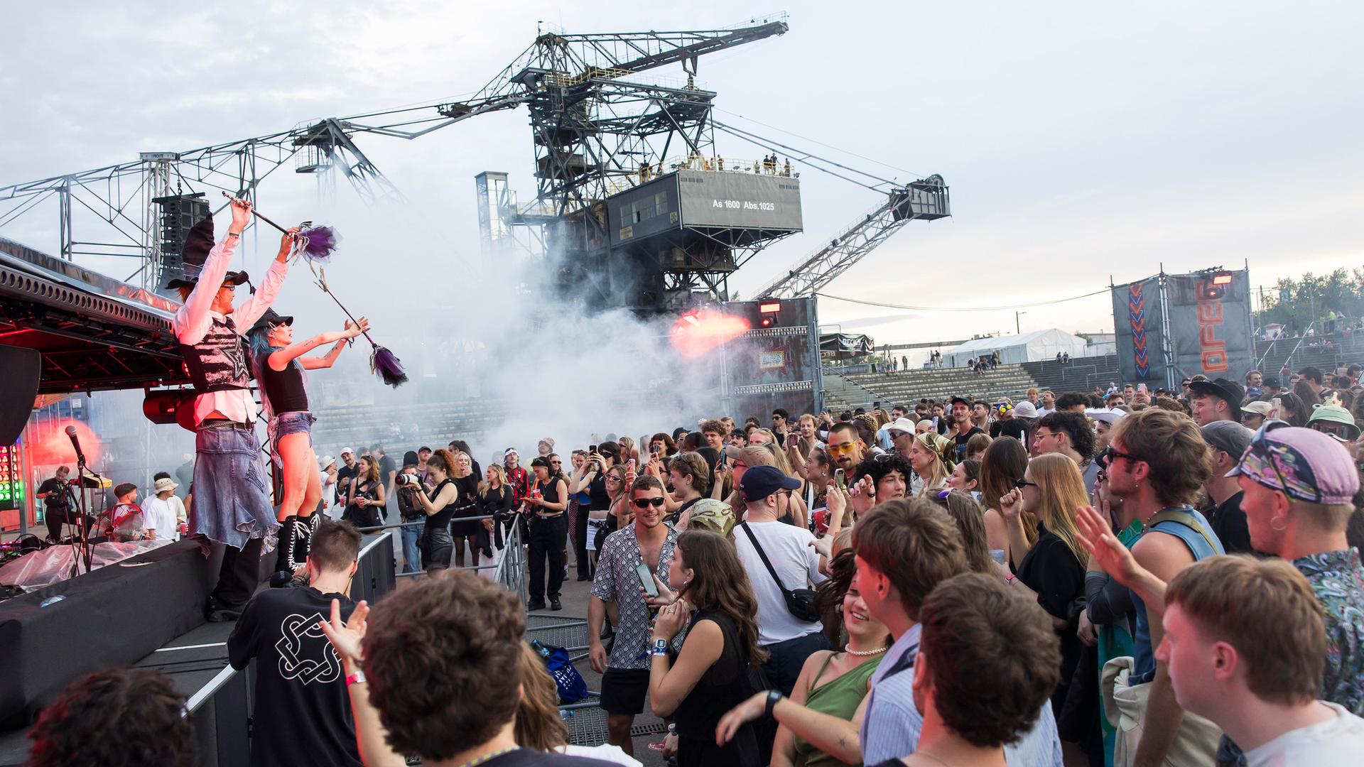 Feiernde Menschen vor riesigen Baggern und einer Bühne mit Musikern beim Melt Festival.