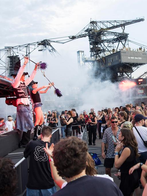 Feiernde Menschen vor riesigen Baggern und einer Bühne mit Musikern beim Melt Festival.