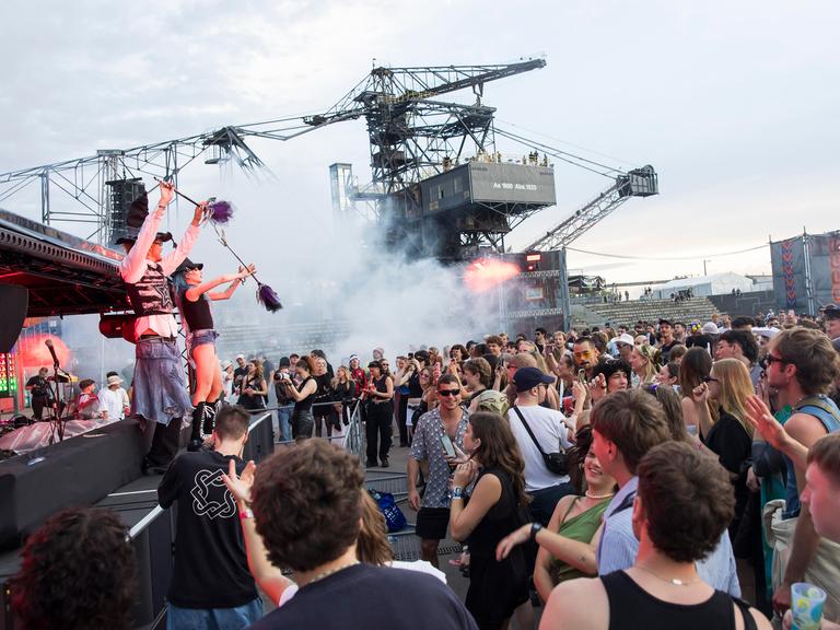 Feiernde Menschen vor riesigen Baggern und einer Bühne mit Musikern beim Melt Festival.