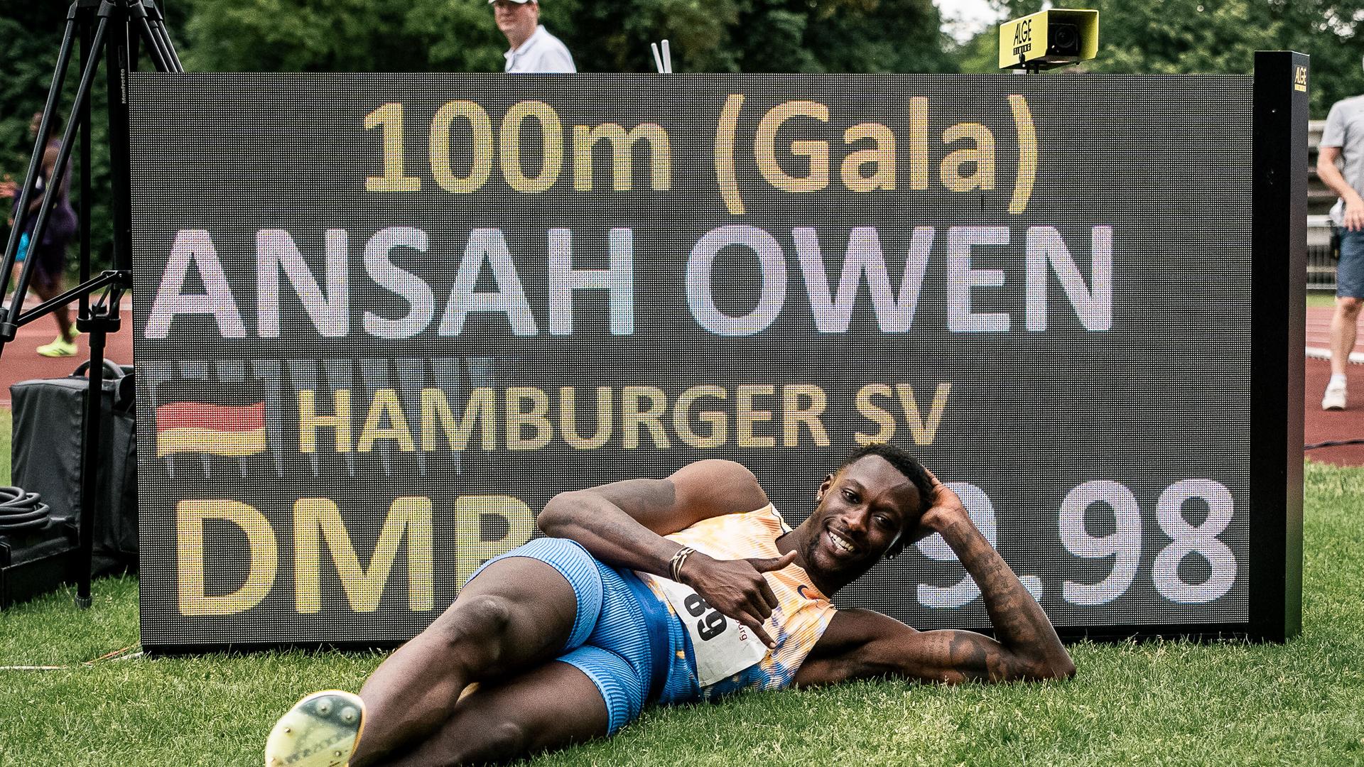 Der Leichtathlet Owen Ansah liegt auf einem Rasen vor einem Schild und zeigt einen Daumen hoch. Auf dem Schild ist zu lesen: 100m, Ansah Owen, Hamburger SV. Der Leichtathlet Owen Ansah liegt auf einem Rasen vor einem Schild und zeigt einen Daumen hoch. Auf dem Schild ist zu lesen: 100m, Ansah Owen, Hamburger SV.