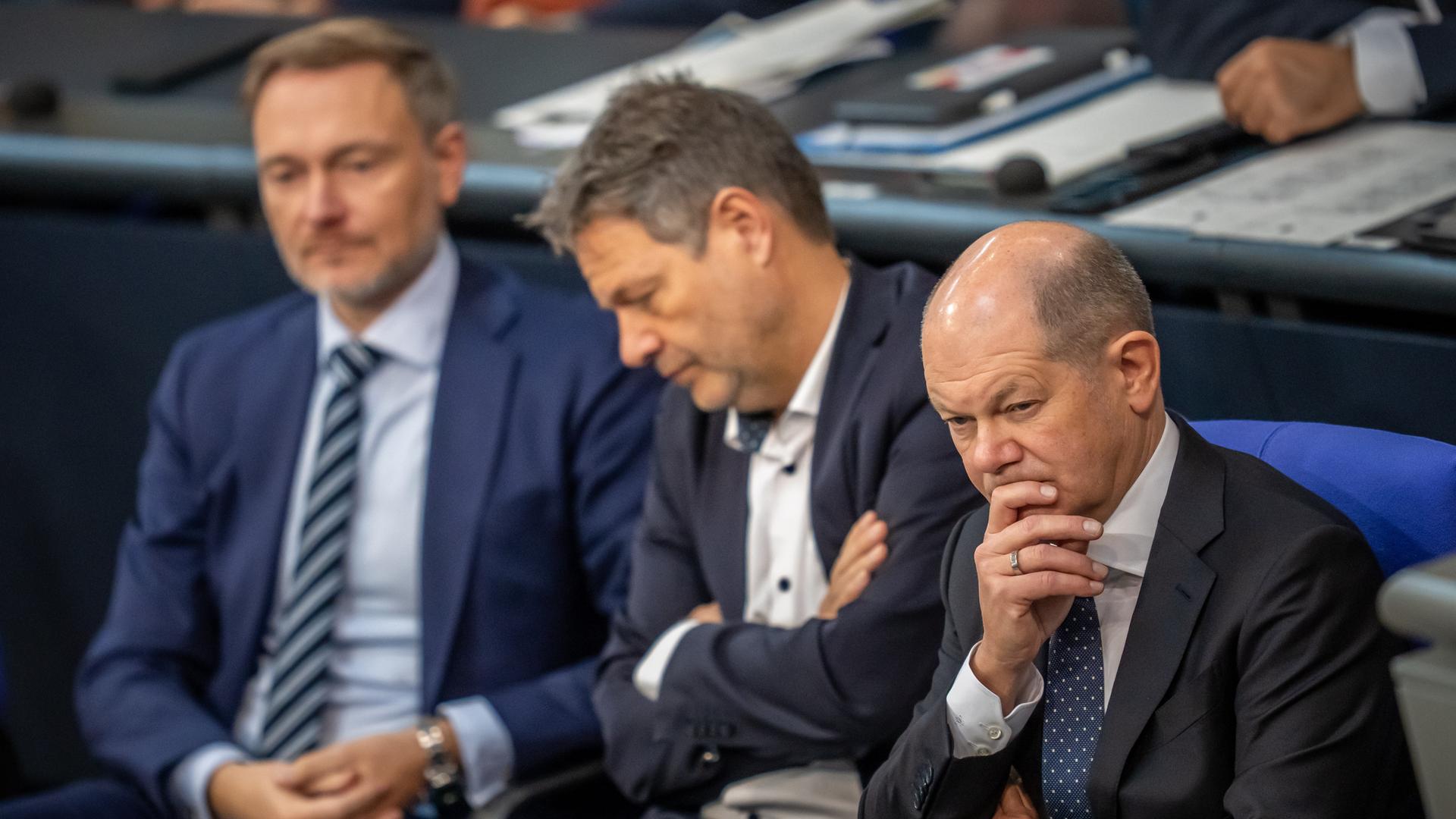 Olaf Scholz, Robert Habeck und Christian Lindner verolgen eine Rede im Bundestag.