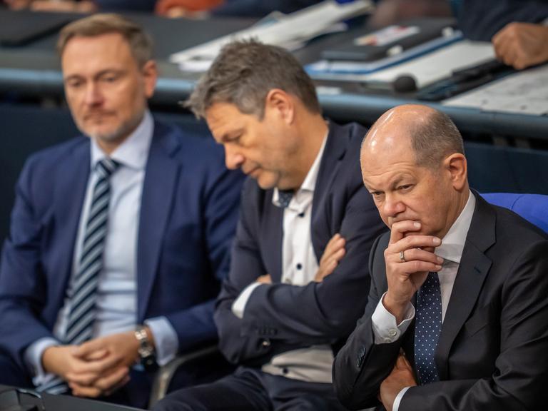 Olaf Scholz, Robert Habeck und Christian Lindner verolgen eine Rede im Bundestag.