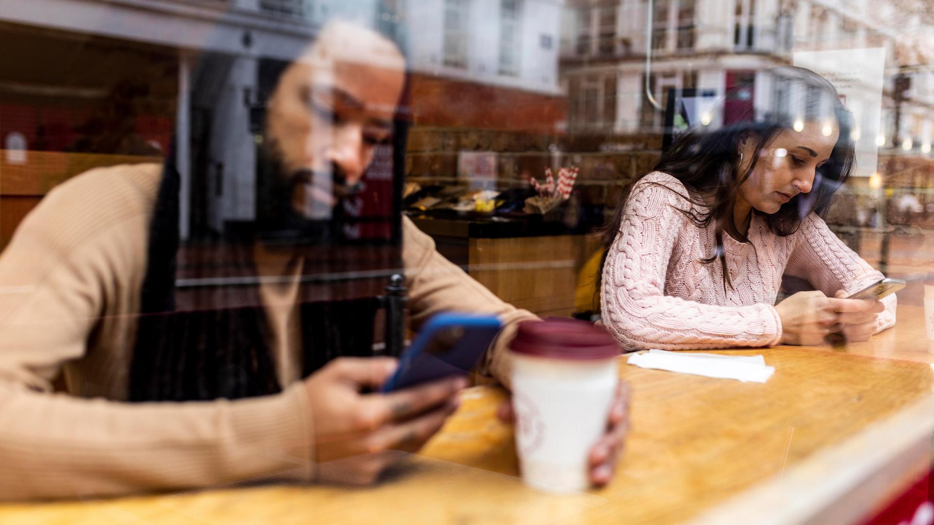 Ein Mann und eine Frau sitzen in einem Café und schauen auf ihre Telefone.