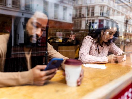 Ein Mann und eine Frau sitzen in einem Café und schauen auf ihre Telefone.