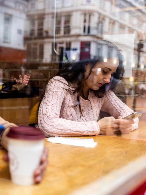 Ein Mann und eine Frau sitzen in einem Café und schauen auf ihre Telefone.