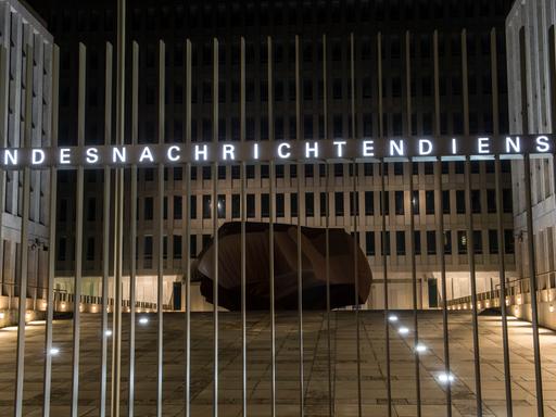 "Bundesnachrichtendienst" steht auf dem Zaun vor einem Gebäudekomplex. Hinter dem Zaun, im Hof, liegt ein Fels. "Bundesnachrichtendienst" steht auf dem Zaun vor einem Gebäudekomplex. Hinter dem Zaun, im Hof, liegt ein Fels.
