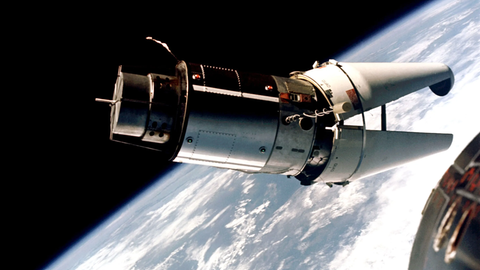 Das Raumschiff Gemini 9 befindet sich im Weltraum über der Erde. Der vordere Teil des Raumschiffs ist geöffnet und sieht dabei so aus, wie das Maul eines Krokodils.
