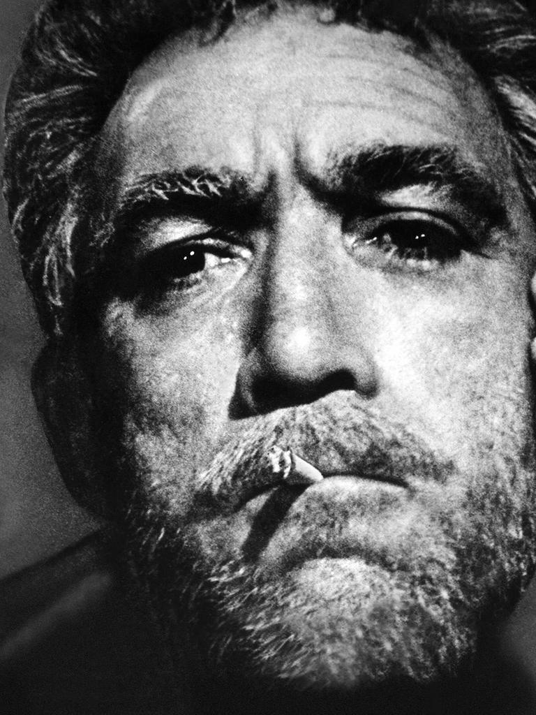 Der Schauspieler Anthony Quinn mit Schauspielerin Eleni Anousaki im Film "Alexis Sorbas". Er hat eine Zigarette im Mund und wird von ihr auf die bärtige Wange geküsst. 
