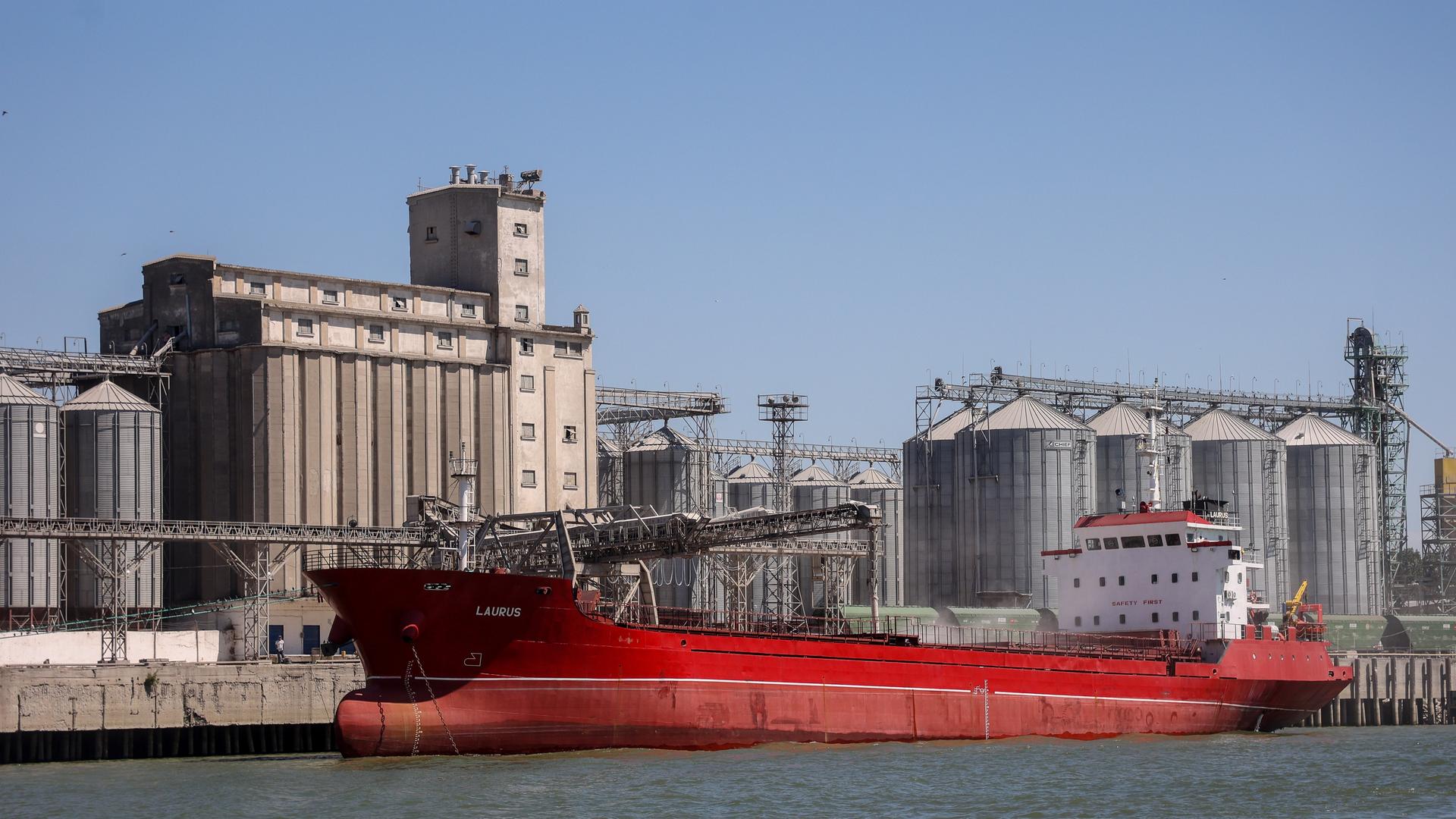 Vor Industrieanlagen am Hafenbecken liegt ein Frachtschiff mit rotem Bug.