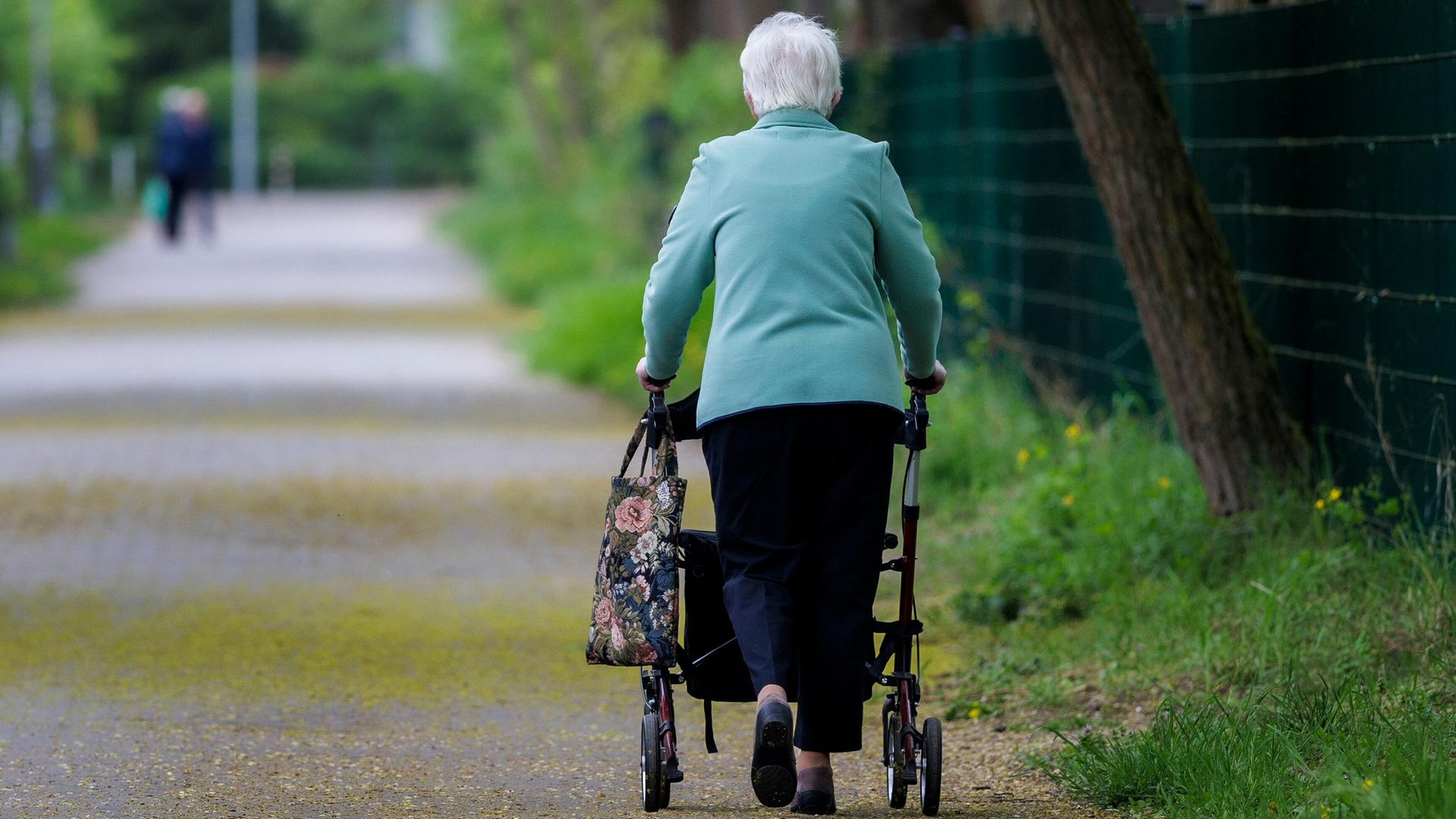  Eine Seniorin läuft mit einem Rollator einen Gehweg entlang.