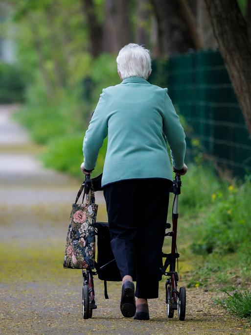  Eine Seniorin läuft mit einem Rollator einen Gehweg entlang.