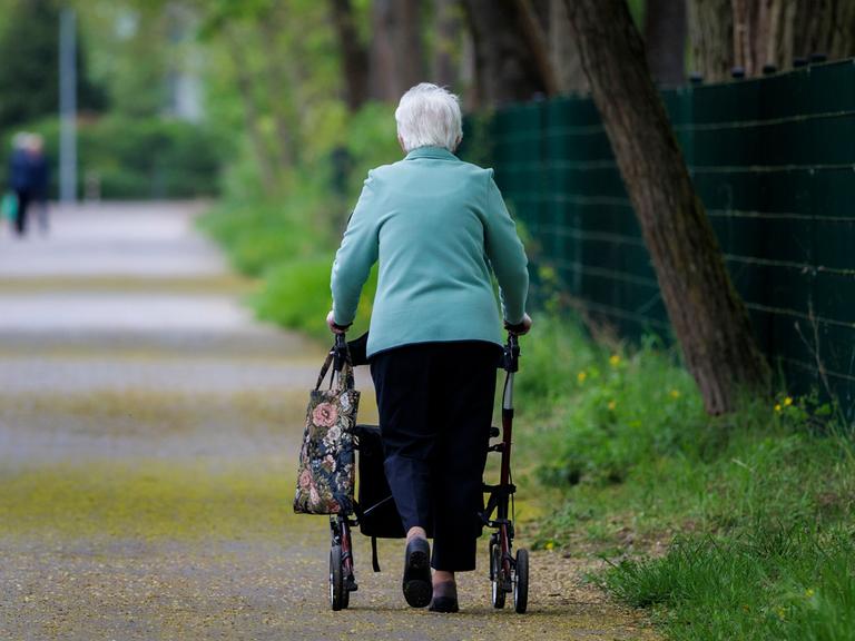  Eine Seniorin läuft mit einem Rollator einen Gehweg entlang.