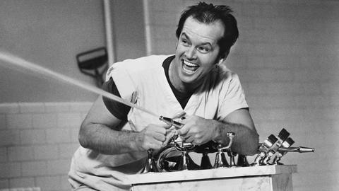 Schwarz-Weißaufnahme von Jack Nicholson, wie er mit einem Wasserschlauch spritzt und sich dabei amüsiert.