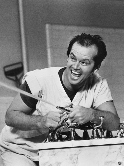Schwarz-Weißaufnahme von Jack Nicholson, wie er mit einem Wasserschlauch spritzt und sich dabei amüsiert.